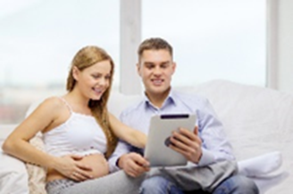 Happy couple looking at a tablet together. One person is pregnant.